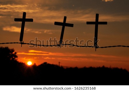 3 wooden crosses on fence at sunset