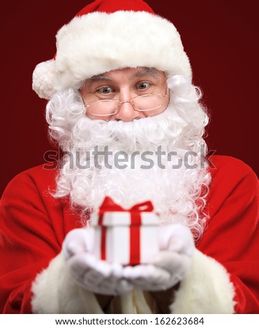 Photo of kind Santa Claus giving xmas present and looking at camera