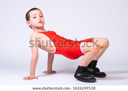 A boy athlete in sportswear and wrestling outfits does an exercise, stands on his arms and legs and looks tiredly at the camera on a white isolated background.