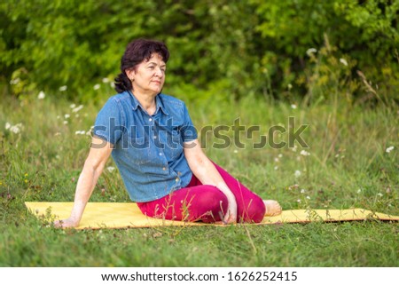 Beautiful mature women sits in Zelenaya Polyana on the mat after gymnastics on a summer day.