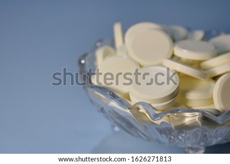 Pills in a glass bowl on a blue background.