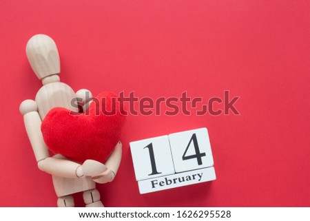 Happy Valentine’s Day card. 14 February wooden calendar and wooden puppet with red heart on a red background
