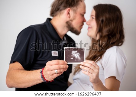 Happy married couple are showing pregnancy test stick and ultrasound picture of their unborn baby. Focus on two stripes