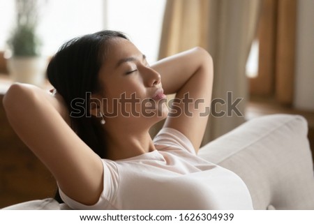 Peaceful young Asian woman relax on couch at home take nap daydream sleep in living room, calm millennial Vietnamese girl sit rest on sofa at home breathe fresh air, peace, stress free concept Royalty-Free Stock Photo #1626304939