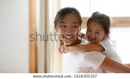 Cute little Vietnamese girl piggyback overjoyed ethnic young mother having fun at home, small smiling Asian daughter child play with happy biracial millennial mom or nanny, entertainment concept Royalty-Free Stock Photo #1626305107