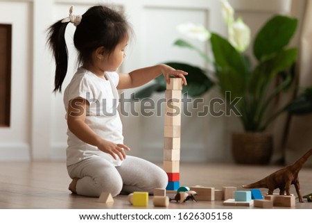 Smart cute little Asian girl sit on warm heated wooden home floor construct with building bricks, small Vietnamese child have fun play with blocks engaged in interesting activity in living room Royalty-Free Stock Photo #1626305158