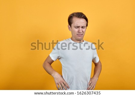 Young man with back pain holding her lower back and neck on yellow background