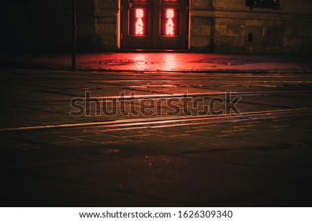 Illuminated by red light cobblestone street at night with bar sign