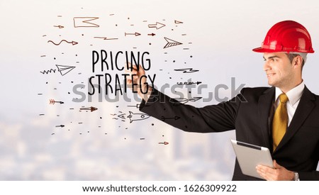 Handsome businessman with helmet drawing PRICING STRATEGY inscription, contruction sale concept
