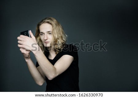 Young man with long blonde hair takes a selfie on a black background.