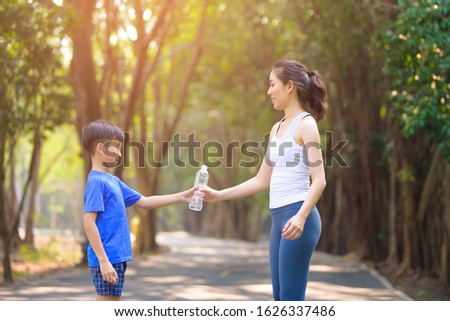 Young Asian boy give a bottle of water to young woman after sport in a park