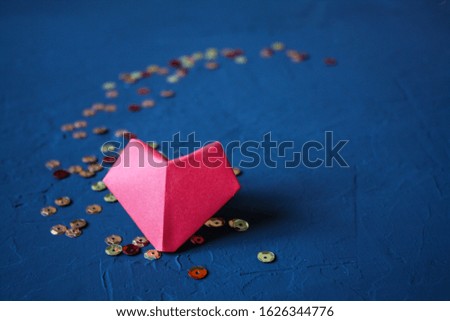 Origami paper heart made of red paper on a dark blue background with sequins.