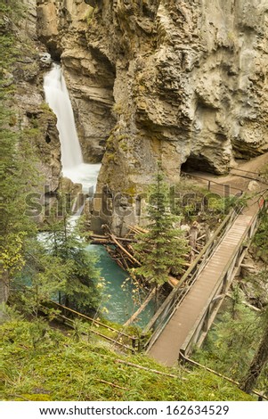 A footbridge over a turquoise pool of glacial water below  Johnston Canyon Lower Falls in Banff National Park, Canada