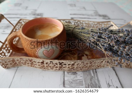 Bouquet of lavender next to a cup of coffee on a wooden background. Cup with a heart and a tray in vintage style. Morning breakfast in bed.