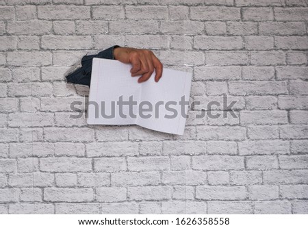 hand sticking through a brick wall with a notebook