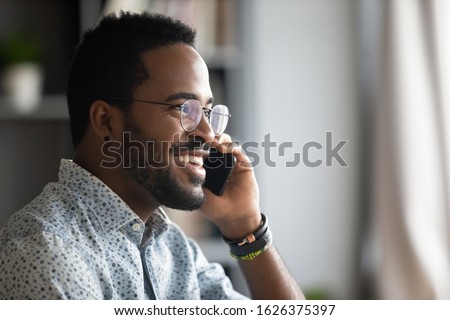 Smiling young adult african american hipster business man professional making business call talking on the phone in office enjoying corporate mobile conversation indoors, closeup side profile view Royalty-Free Stock Photo #1626375397