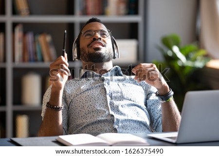 Millennial african american businessman student worker wear wireless headphones listening music at workplace, relaxed male ethnic professional enjoying songs podcast chill at home office work desk Royalty-Free Stock Photo #1626375490