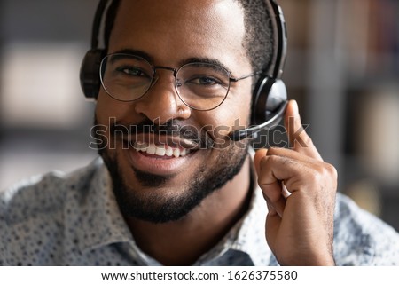 Happy friendly african ethnic business man telemarketing operator wear wireless headset microphone looking at camera, customer support service assistant on call center phone closeup headshot portrait Royalty-Free Stock Photo #1626375580