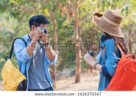 Young Asian Man using film camera taking photo of his girlfriend while traveling together at park. outdoor and travel concept.