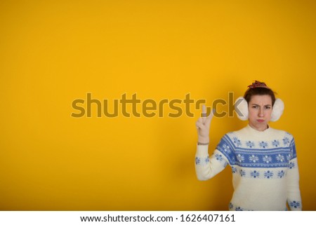 portrait of a serious woman in winter clothes showing signs with fingers on a yellow background