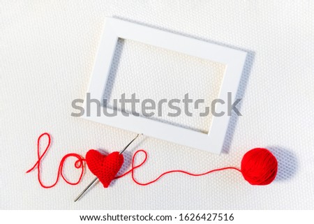 Valentine's day or wedding backdrop. Red knitted volume heart in word love, ball of thread and white frame on knitted background. Template for design, valentines card, invitation. Mock up Top view.