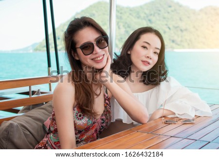 Two asian beautiful women are talking and relaxing while sitting on a boat with blur background of blue sea and mountains