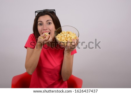 woman with 3D glasses on her head sits on a chair eating movie popcorn
