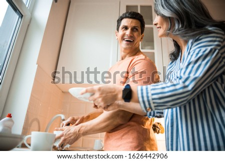 Cropped photo of smiling adult man and woman washing dishes together at home stock photo