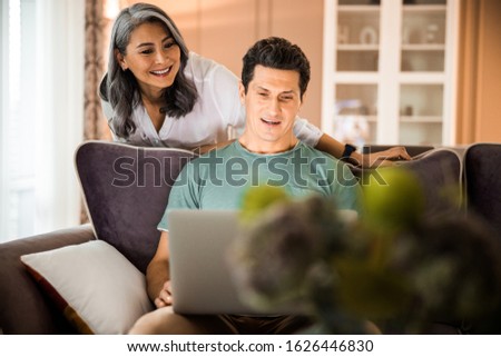 Happy adult man sitting on sofa while her wife staying next to him stock photo