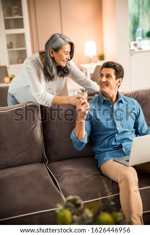Smiling beautiful wife offering water to her husband at home stock photo