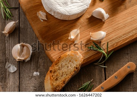 Baguette bread, garlic, rosemary and Brie cheese. Food flat lay on wooden background.