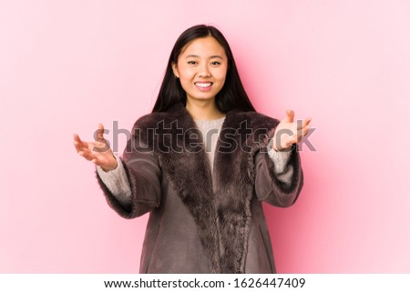 Young chinese woman wearing a coat isolated feels confident giving a hug to the camera.