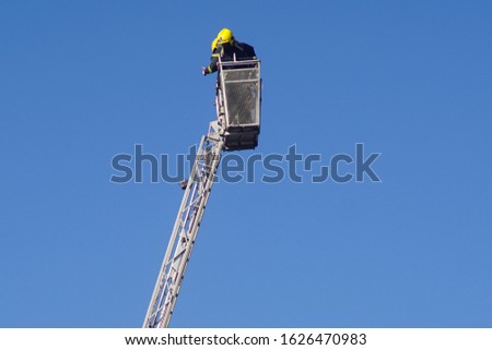 Fire rescue basket with fire fighters on end of hydraulic arm. Blue background.                          