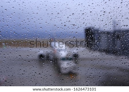 bad weather at airport. rain water droplets caught on airport terminal window and blurred out of focus picture of airplane dock and loading cargoes while passenger wait for boarding.