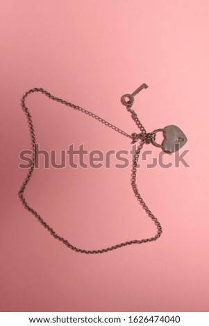metal heart with a key on a chain on a pink background