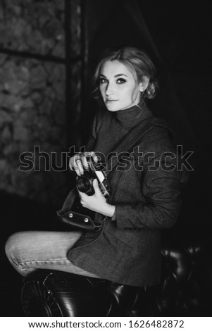 Beautiful woman blonde photographer in a strict suit holds in his hands the old retro camera. Black and white photo.