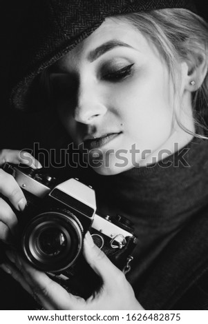 Beautiful woman blonde photographer in a strict suit and a cappie is holding an old retro camera in her hands. Soft focus. Black and white photo.