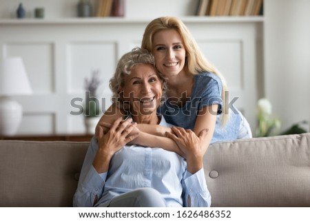Portrait of happy affectionate young woman cuddling sitting on sofa smiling mature retired mother. Attractive two female generations family looking at camera, showing love care support at home. Royalty-Free Stock Photo #1626486352