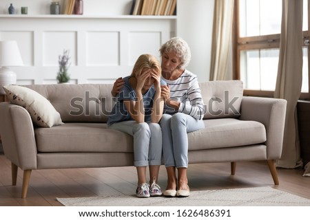 Full length compassionate older mother embracing shoulders of depressed adult child, sitting together on couch. Empathic middle aged mother showing support care to grown up daughter, sharing pain. Royalty-Free Stock Photo #1626486391