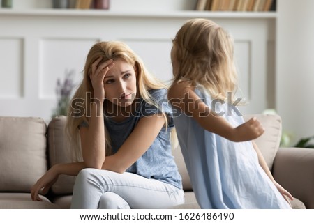 Stressed young woman nanny irritated by loud hyperactive little preschool kid girl at home. Unhappy exhausted mother suffering from small screaming child daughter demanding attention at home. Royalty-Free Stock Photo #1626486490
