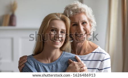Head shot close up happy hoary woman embracing attractive grown up daughter, looking at camera. Portrait of pleasant loving two female generations family with good relations, enjoying sweet moment.