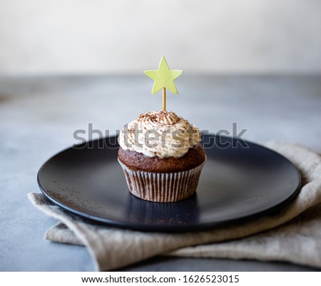 chocolate cupcake with cream on a dark plate, for a birthday or celebration. light gray background. vertical image.