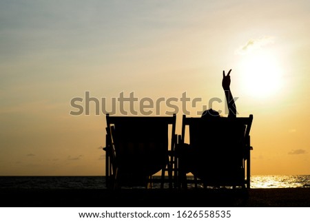 man showing  two finger peace sign while sitting on a deck chair on a beach in a sunrise moment