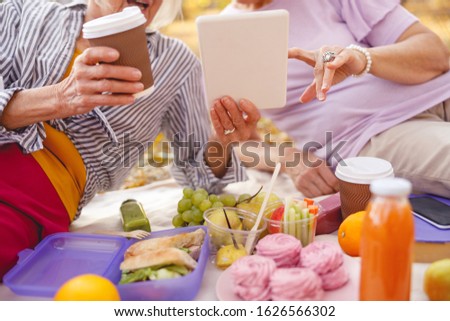 Close up picture of a tablet in hands of an aged woman having picnic with her mate