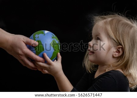Mother gives the planet into the hands of a child. Isolated on dark background.