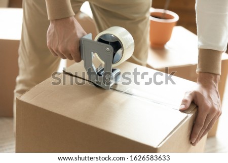 Close up of man sealing packing cardboard box with scotch tape moving or relocating, Caucasian husband roll carton package personal belongings using adhesive cellotape, relocation service concept Royalty-Free Stock Photo #1626583633