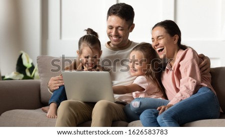 Overjoyed young family with small kids relax on couch in living room laugh watch funny video on laptop, excited happy parents rest have fun with little daughter use computer, enjoy home weekend