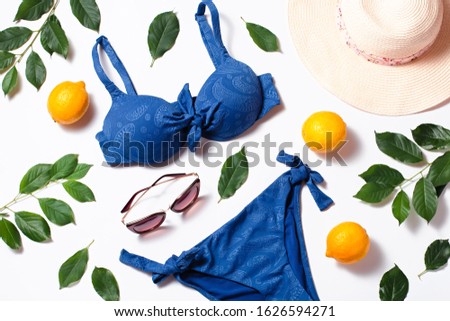 Travel flat lay with classic blue color swimsuit, green leaves and lemons. Nature friendly flat lay with beach fashion accessories and natural elements on white background. Blue and yellow tones