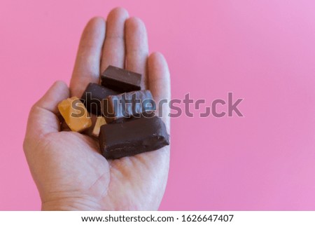 Hand with chocolates on a pink background. Enjoying sweets. Sweet addiction concept. The concept of love for sweets. copy space