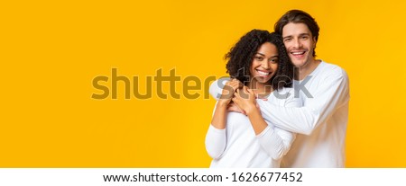 Happy interracial couple portrait. Joyful mixed-race sweethearts embracing and posing to camera, standing together on yellow background, panorama